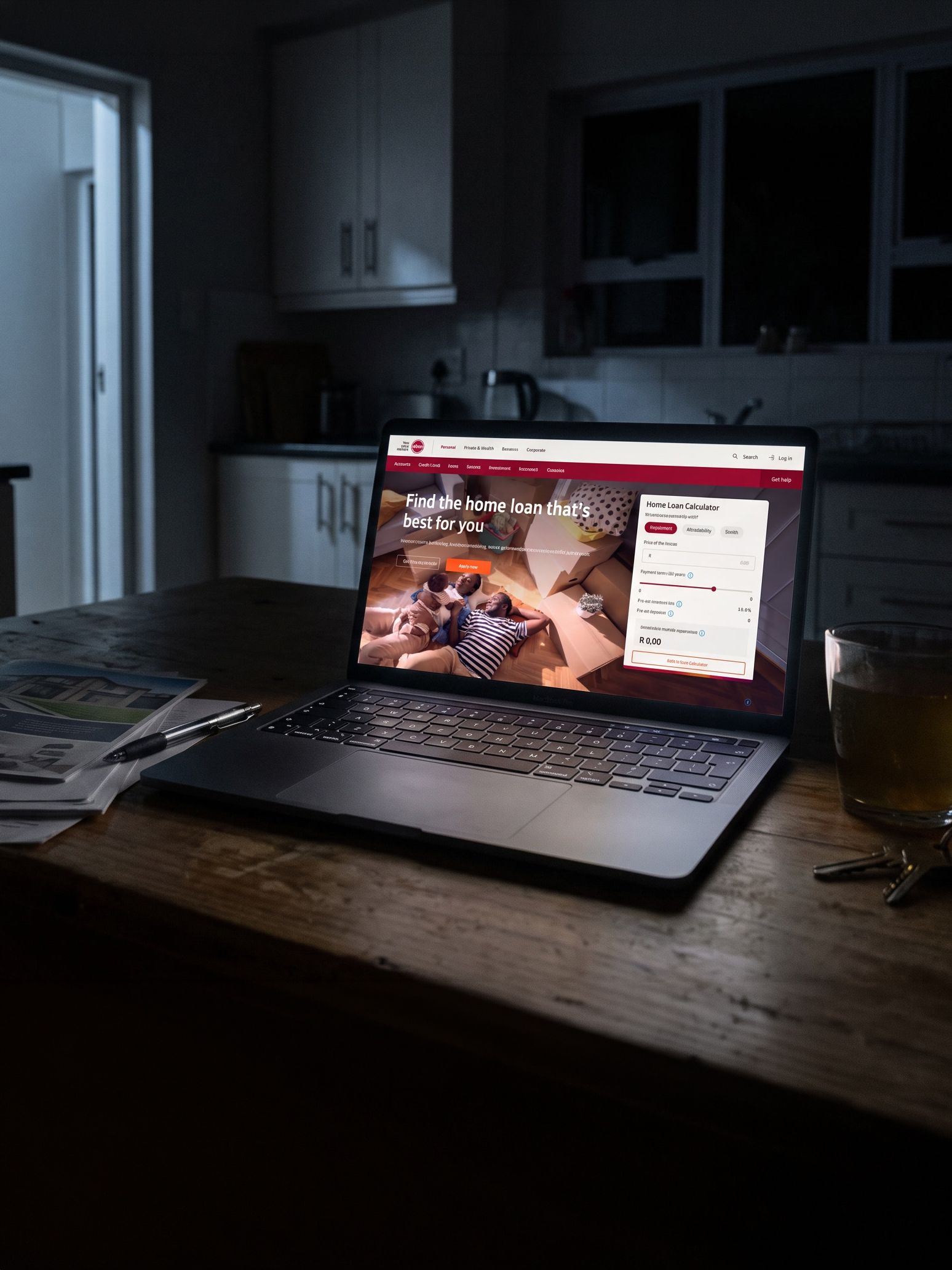 A MacBook Pro open on a dark kitchen table late at night, the screen the only light in the room, a glass and a set of keys beside it and printed property listings under a pen. On the screen is the Absa home loans page: the heading Find the home loan that’s best for you over a photograph of a family among cardboard moving boxes, with the Home Loan Calculator panel sitting in the hero beside it.