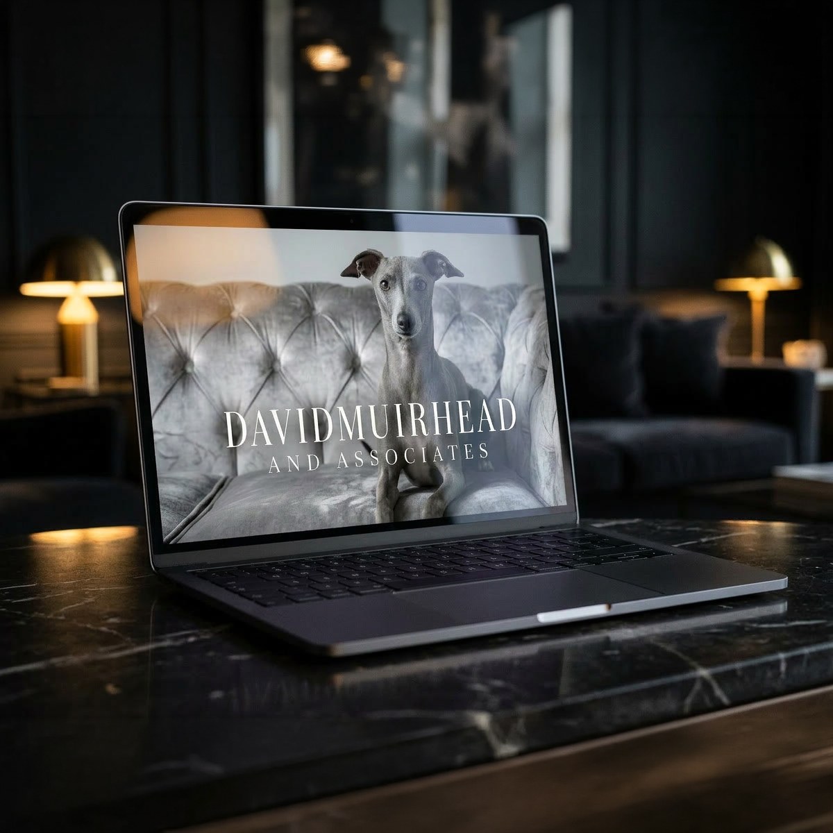 The David Muirhead site open on a laptop in a dark lounge, the whippet and wordmark filling the screen.