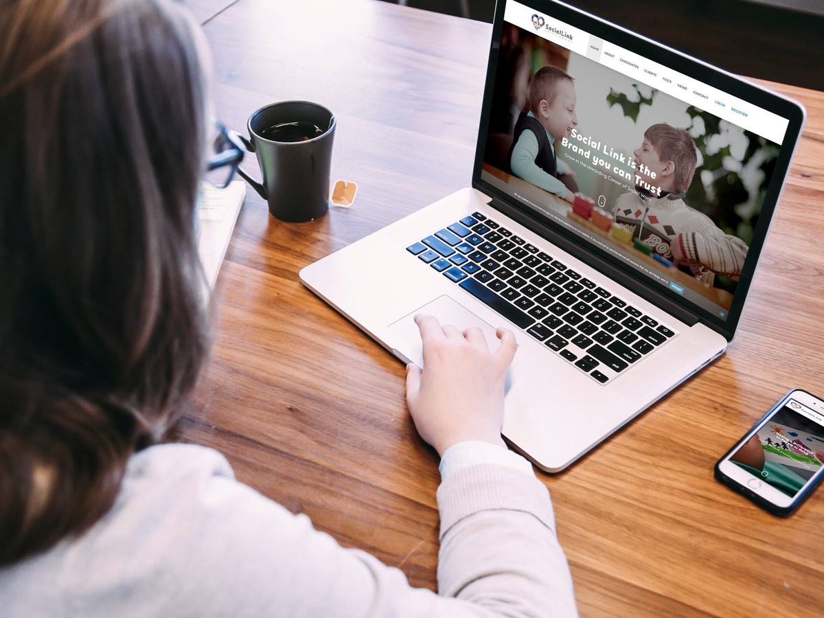 Someone at a desk viewing the Social Link site on a laptop, a phone showing the same site beside it.