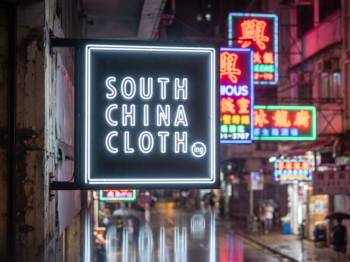 The South China Clothing mark as a white neon blade sign over a wet Hong Kong street at night.