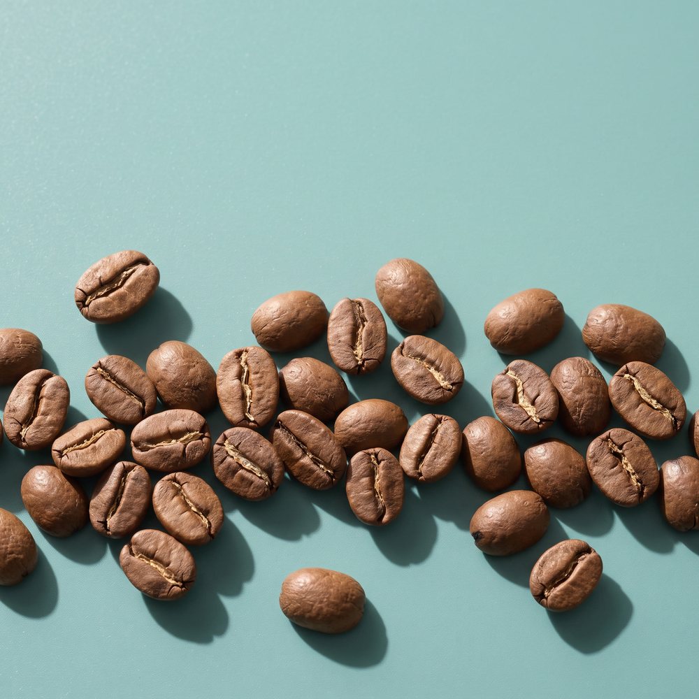 Roasted coffee beans scattered across a duck-egg teal surface.